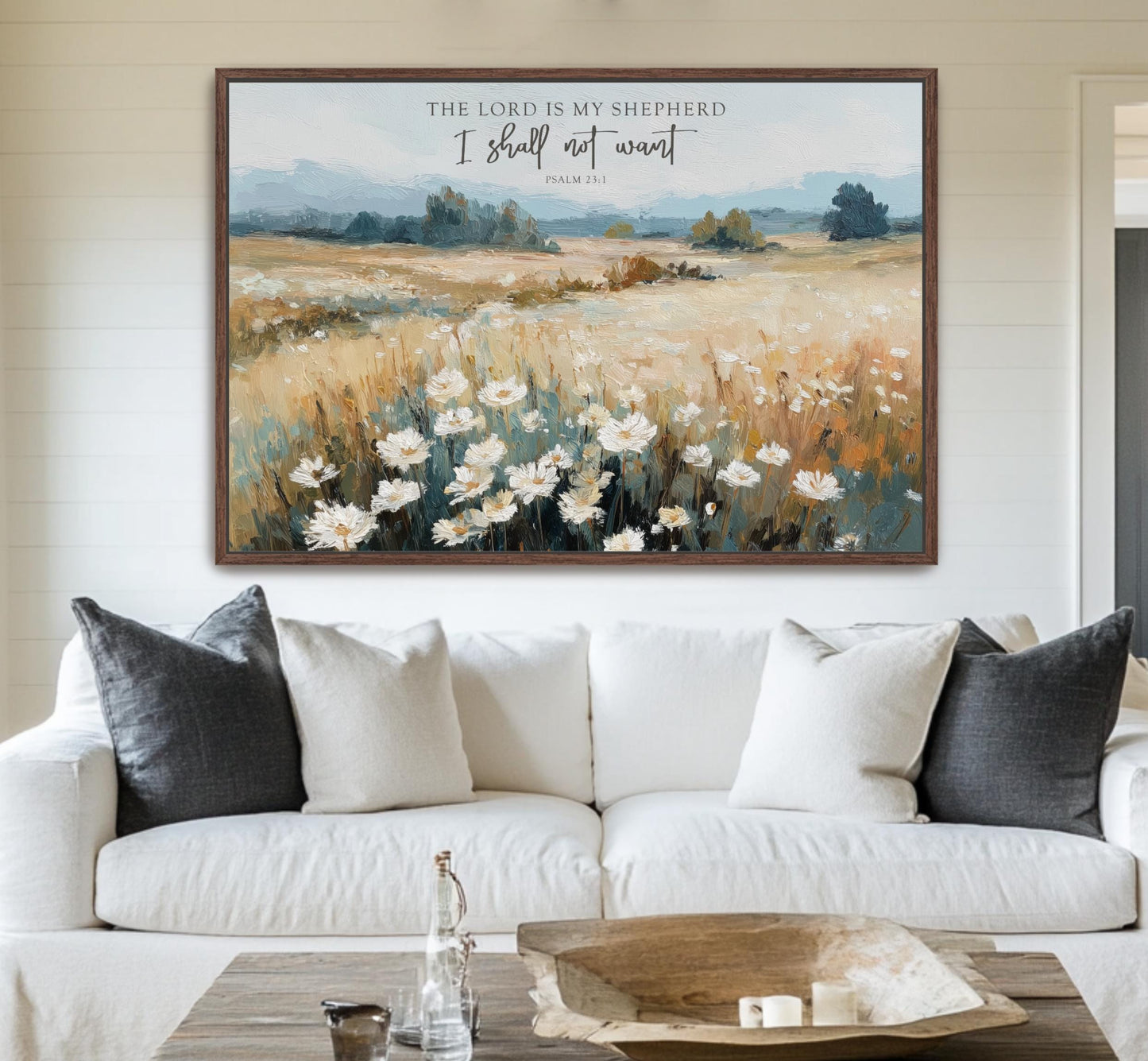 a large framed painting of a field with white flowers hanging on a wall above a white couch with gray pillows.