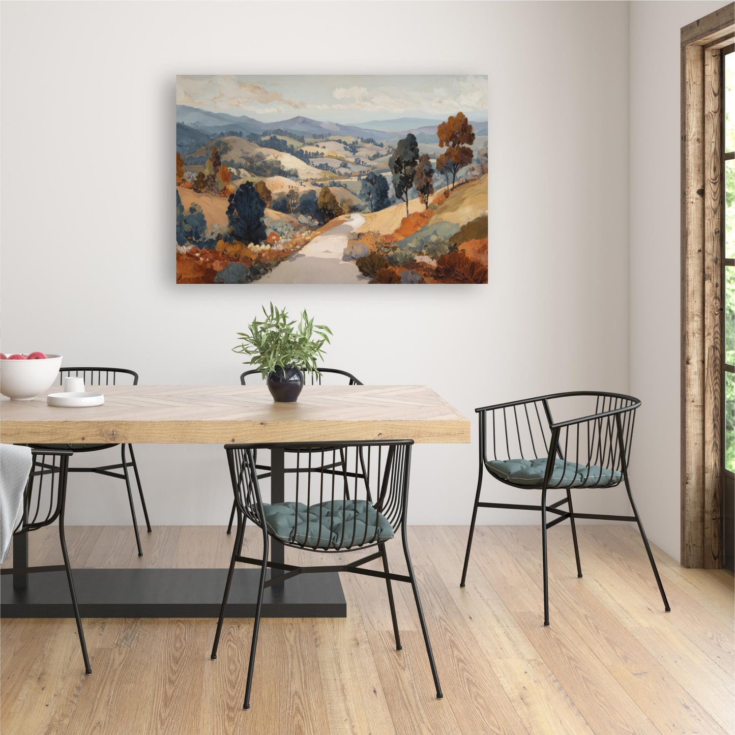 a dining room with a wooden table and chairs, a painting of a countryside landscape hanging on the wall, and a potted plant on the table.