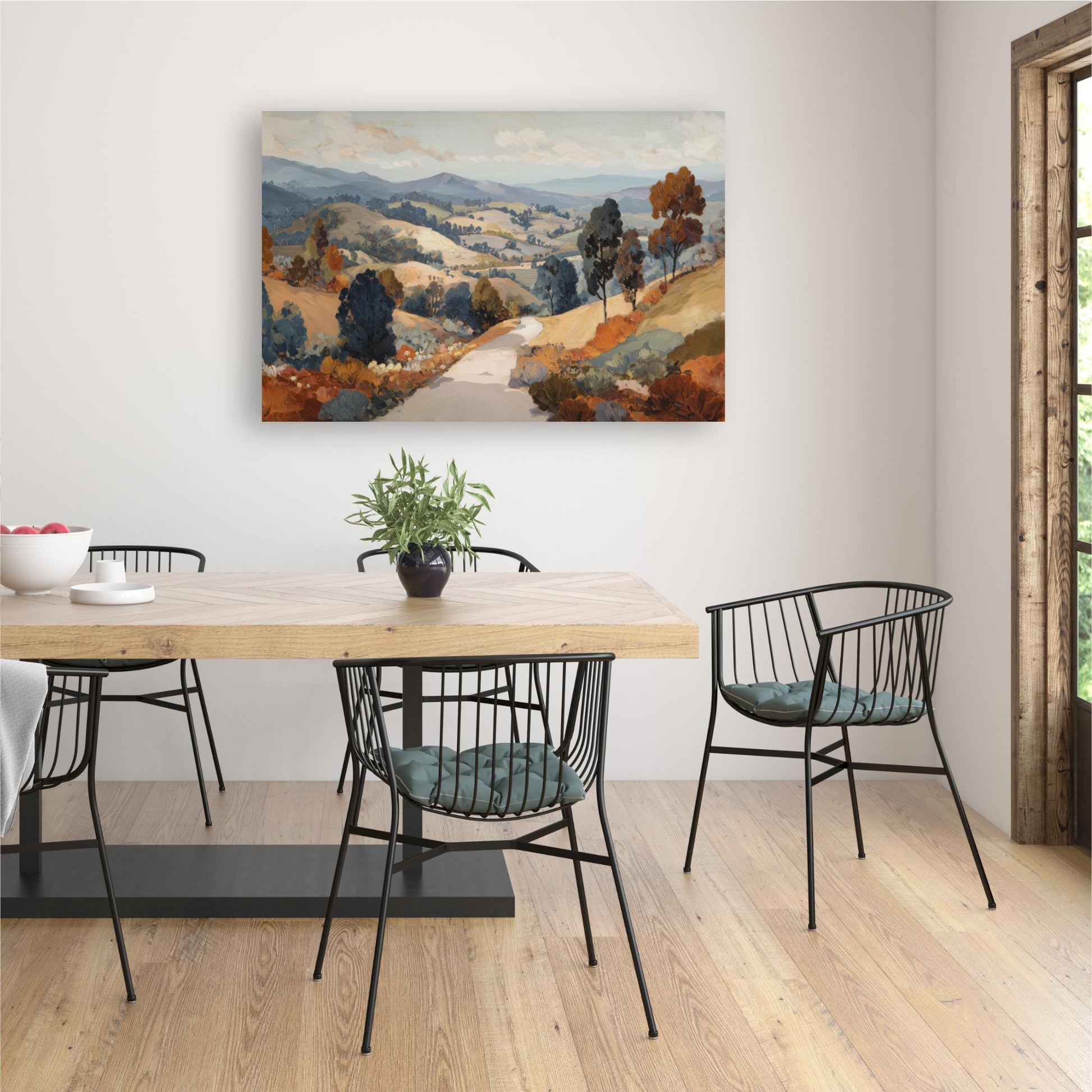a dining room with a wooden table and chairs, a painting of a countryside landscape hanging on the wall, and a potted plant on the table.