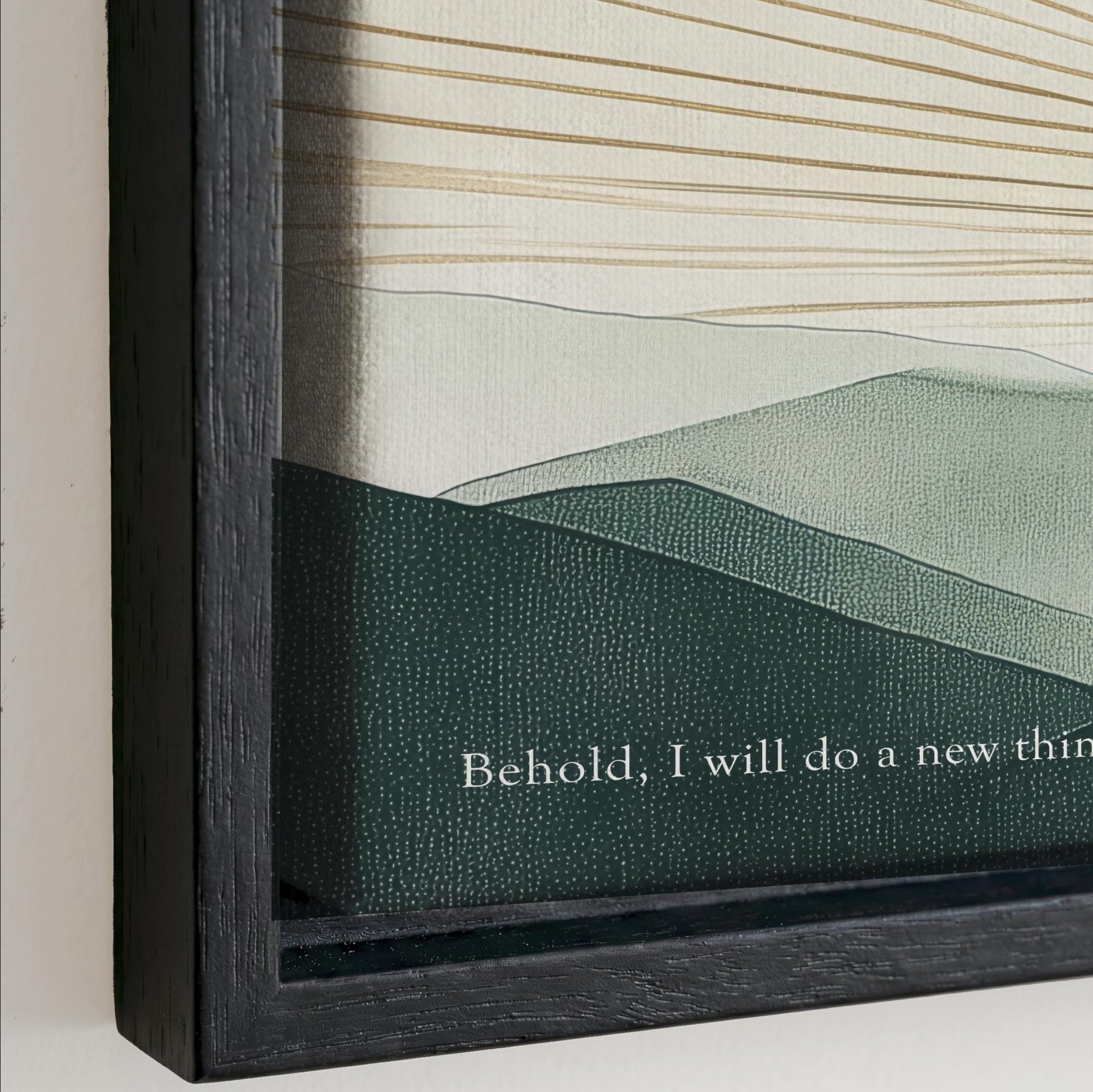 The image is a framed artwork depicting a landscape with mountains and hills. The text on the frame reads "Behold, I will do a new thing".