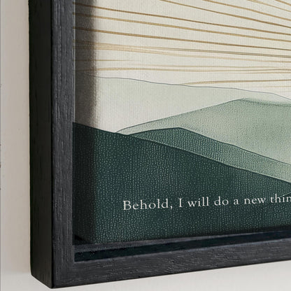 The image is a framed artwork depicting a landscape with mountains and hills. The text on the frame reads "Behold, I will do a new thing".