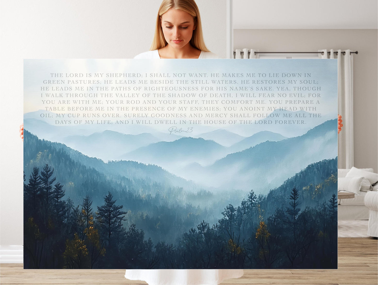 A woman holds a large canvas print of a serene mountain landscape with trees and fog, featuring a biblical verse from the book of Proverbs.