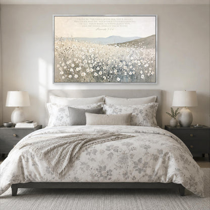 a serene bedroom scene with a large bed adorned with a floral comforter and pillows, flanked by two nightstands with lamps. Above the bed, a large framed painting of a field of flowers is displayed on the wall, creating a peaceful and calming atmosphere.